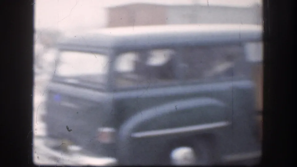 Soft 8mm frame of a dark mid-century car in snowy conditions, with window framing and faded color from the home-movie scan.