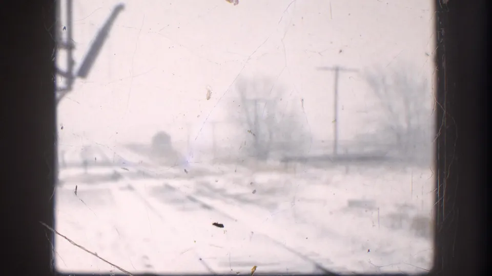 Soft 8mm winter road view in Kansas, with snow-covered ground, utility poles, bare trees, and film scratches.