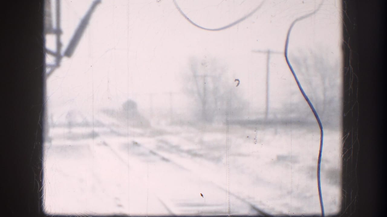 Snow-covered train tracks seen through a dark window frame on an overcast day.