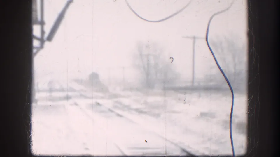 1958 Kansas home-movie frame showing snowy rail tracks, bare trees, and utility poles viewed through a window.