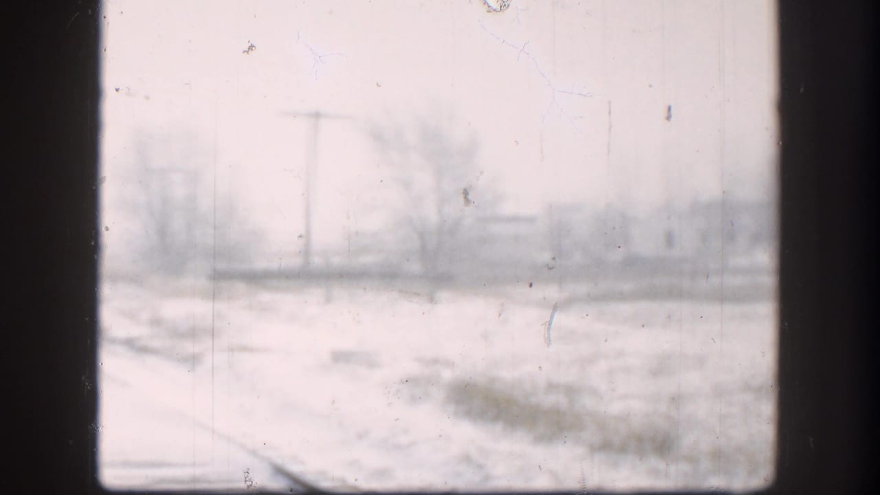 Pale snowy rail corridor with utility poles and distant trees behind a dark window edge.