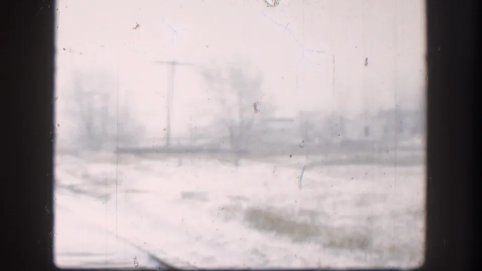 Soft 8mm view of a snowy Kansas rail corridor in 1958, with utility poles, bare trees, and winter haze.