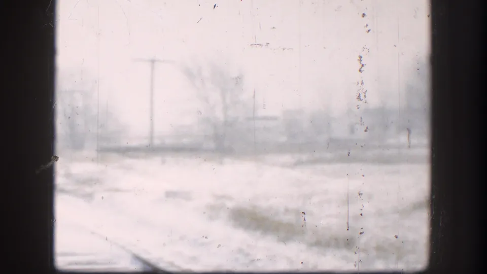 1958 Kansas winter frame with soft-focus snow, a utility pole, bare trees, and rail tracks partly visible below.