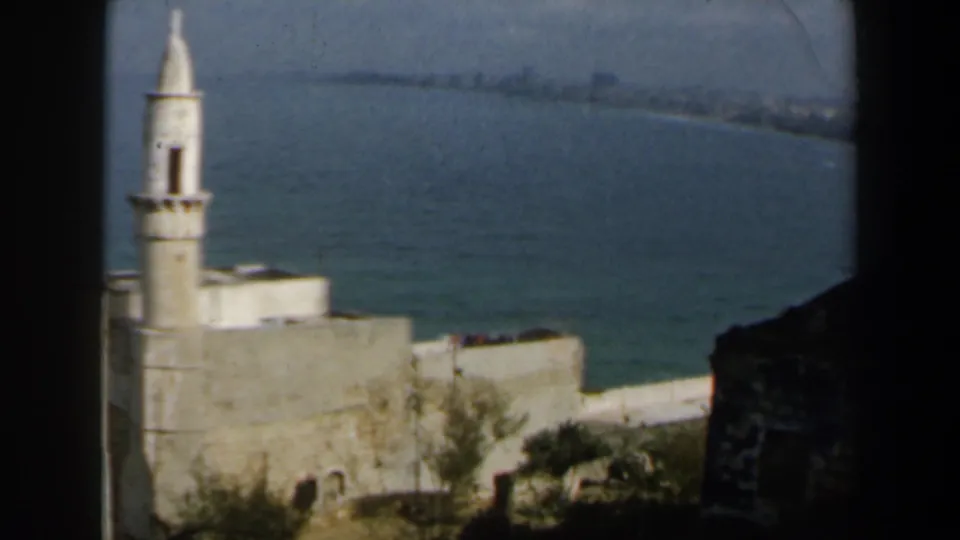1960 Israel coastal view centered on a white minaret, pale buildings, and blue sea under a hazy sky.