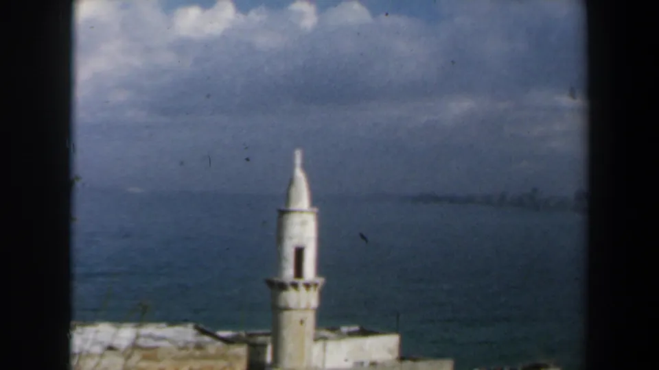 1960 Israel home-movie frame of a white minaret near the sea under a cloudy sky.