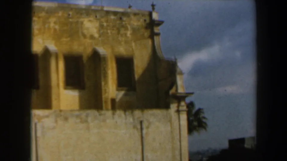 1960 Israel 8mm frame of a weathered stone structure with arched openings, parapet details, and a small tower form near the edge.