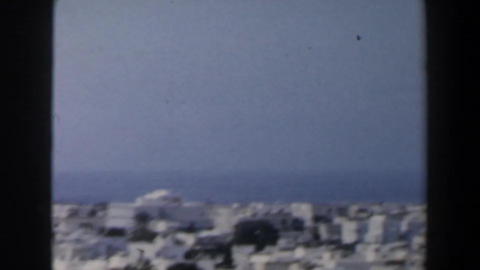 Elevated 1960s Israel view over pale city buildings toward the sea and a ship on the horizon.