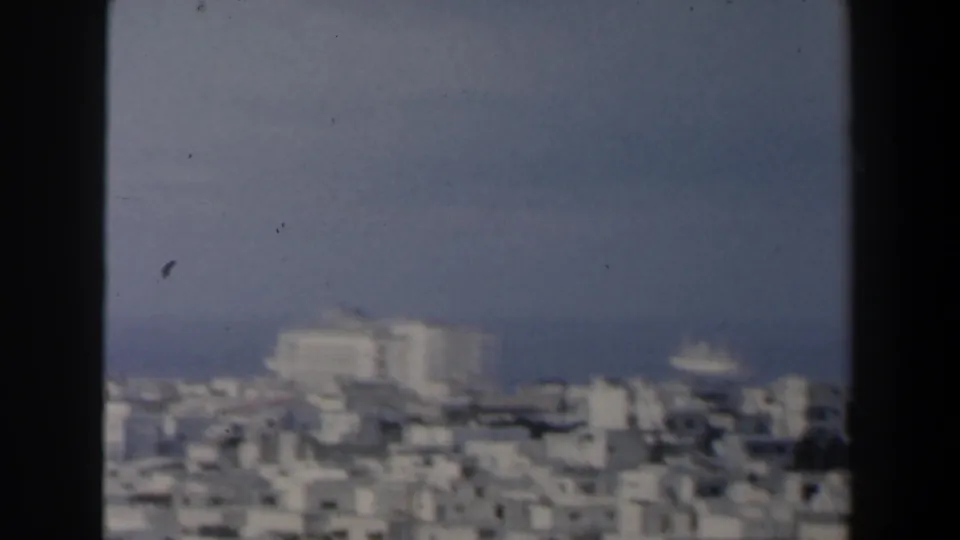 Soft 8mm frame of dense pale buildings, harbor water, and a ship offshore in Israel, based on clip metadata.