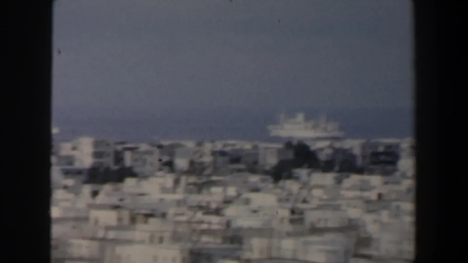 1960 Israel 8mm frame showing a hazy coastal city panorama with white rooftops, sea horizon, and a distant vessel.