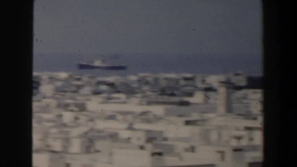 Elevated 1960 Israel coastal view framed by dark edges, with pale buildings below and a ship on the blue horizon.