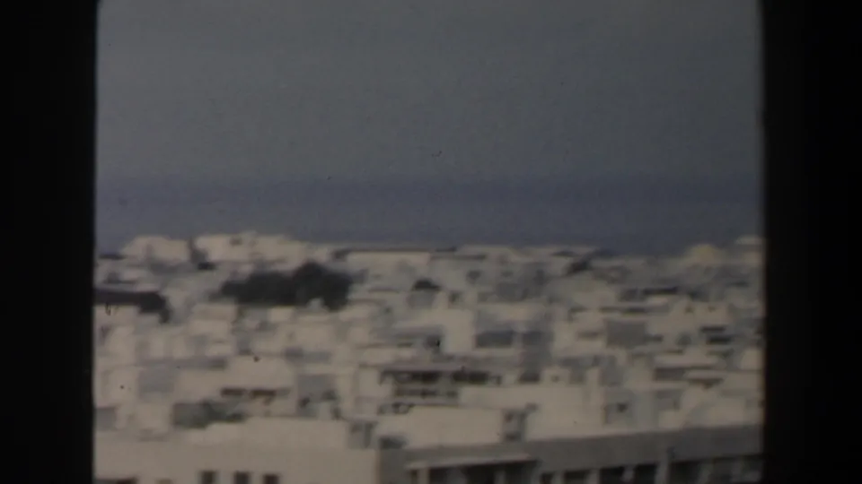 Late frame from the 1960 Israel coastal panorama, showing clustered white buildings beneath a hazy blue sea horizon.