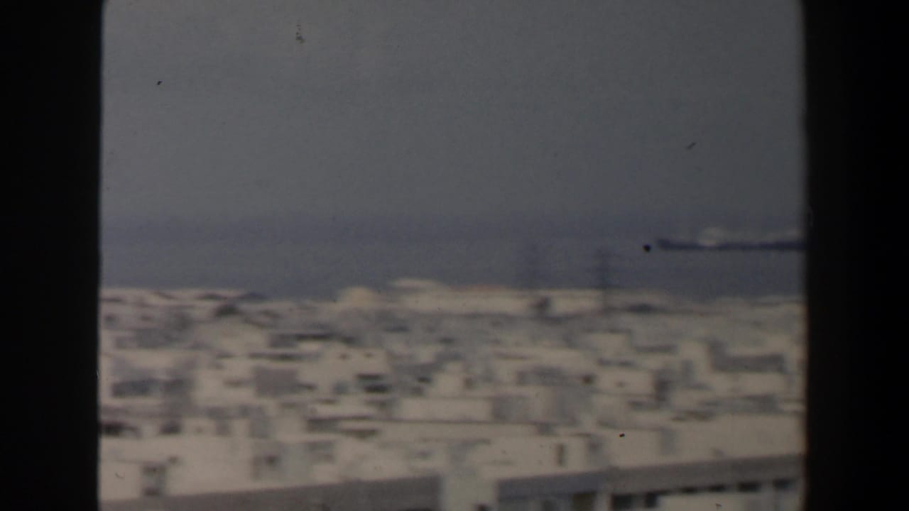 1960 Israel home-movie frame showing white urban rooftops and a hazy coastline from an elevated viewpoint.