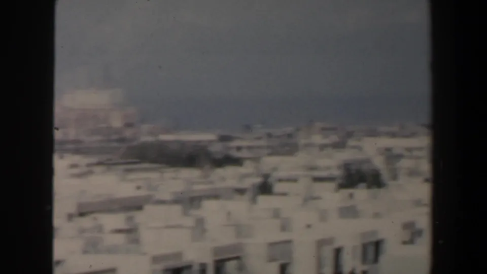 1960 Israel home-movie still looking over low white buildings near a muted coastal horizon.