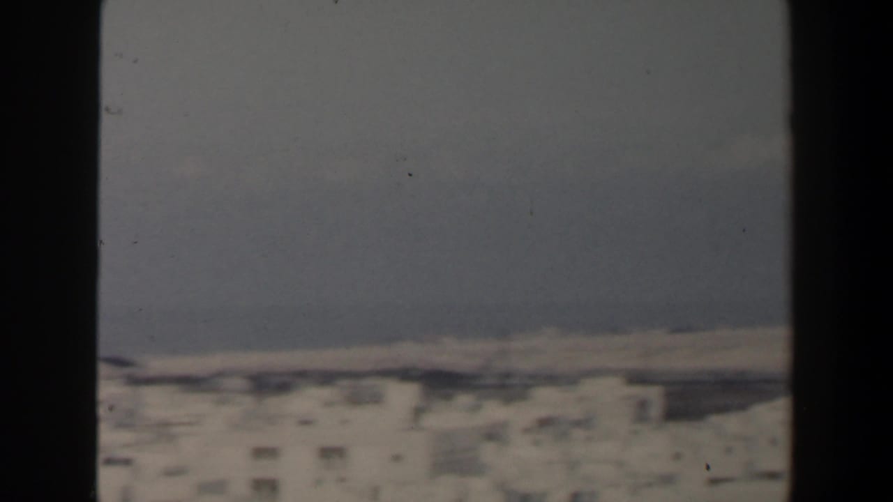1960 Israel 8mm frame showing a hazy elevated view of pale city buildings and distant shoreline through dark window trim.