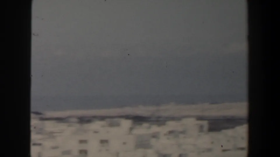 1960 Israel 8mm frame showing a hazy elevated view of pale city buildings and distant shoreline through dark window trim.