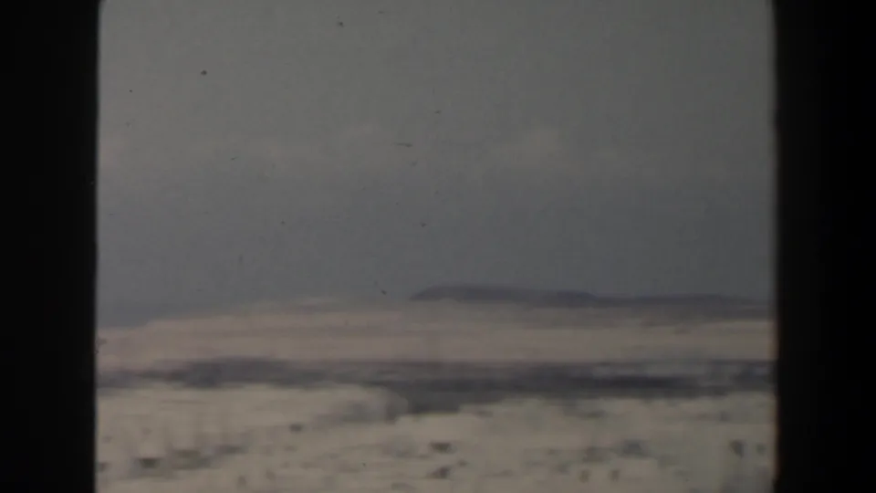 Soft 8mm view of a small Israeli city skyline, with pale buildings below a hazy sky and faint landforms on the horizon.