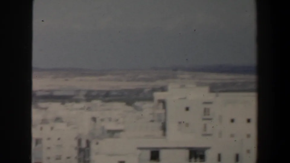 Elevated 1960 Israel home-movie frame showing white low-rise buildings, a hazy horizon, and dark window trim at the sides.