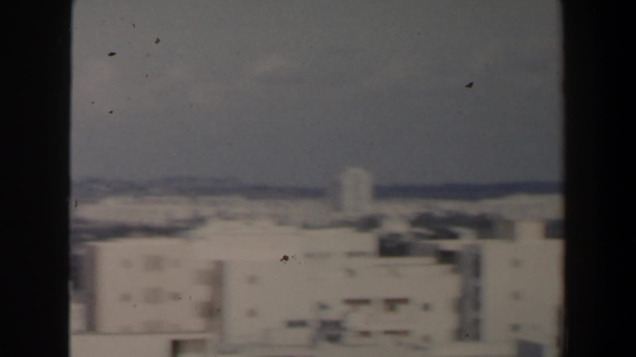 1960 home-movie view of a hazy Israeli city with pale rooftops and distant landscape behind dark vertical borders.