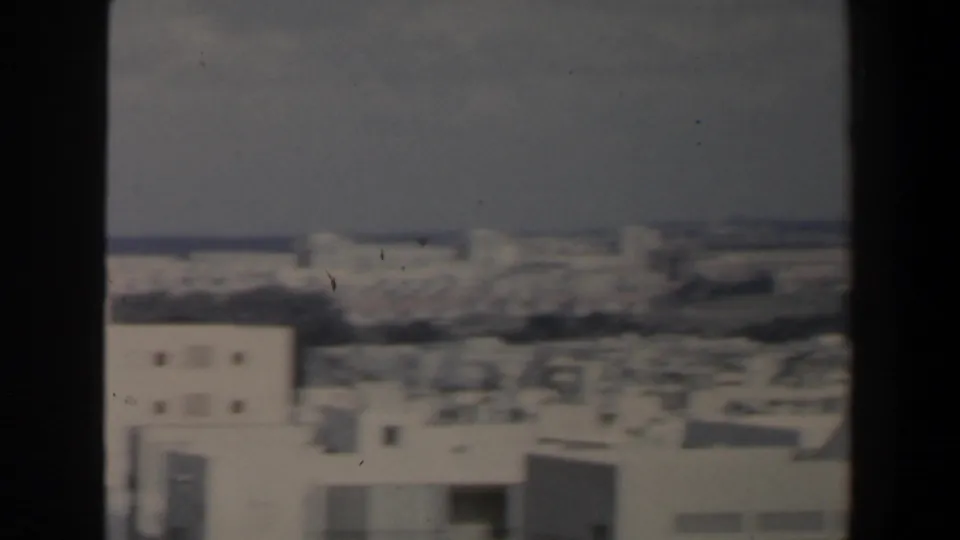 Hazy 1960 Israeli urban skyline with flat-roofed buildings, soft focus, and dark vertical framing at both sides.