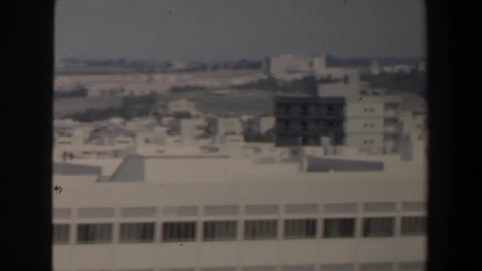 Elevated 1960 Israel city view showing a large white building, nearby blocks, rooftops, and distant landscape.