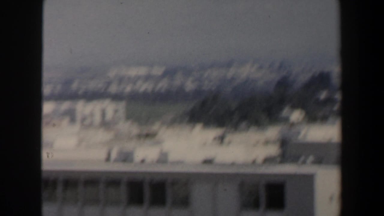 Soft-focus city view with pale buildings in the distance and dark vertical framing through the center.