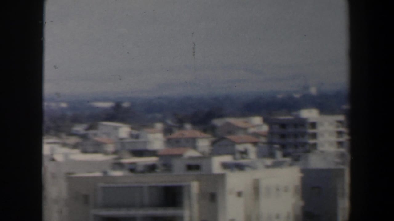 1960 Israel 8mm frame showing a soft aerial view over white apartment blocks, rooftops and distant trees.
