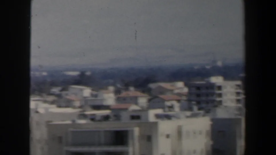 1960 Israel 8mm frame showing a soft aerial view over white apartment blocks, rooftops and distant trees.