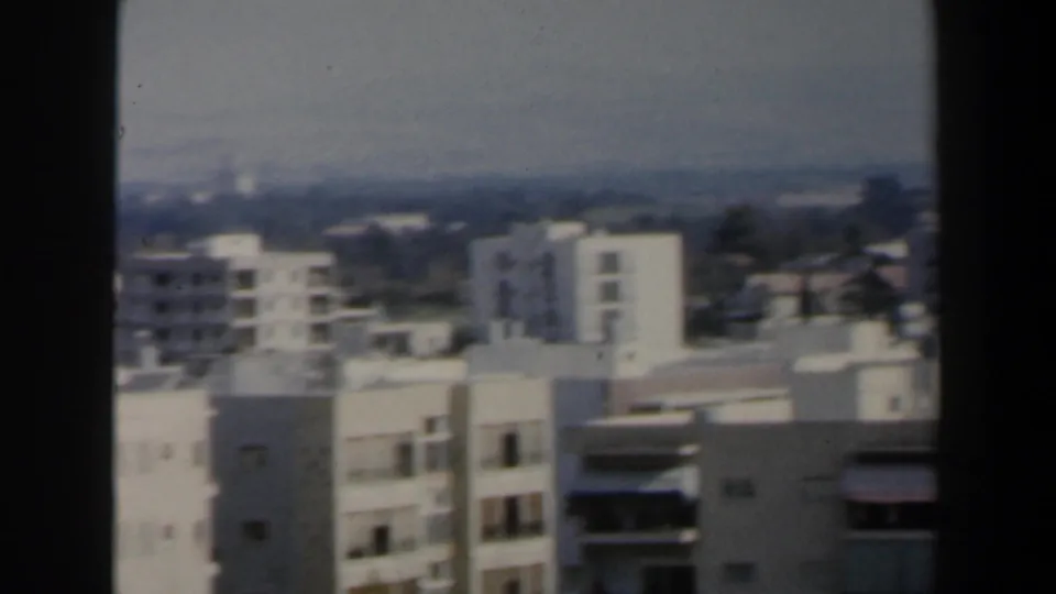 1960 Israel home-movie frame looking over white high-rise apartments, balconies and a distant hazy skyline.