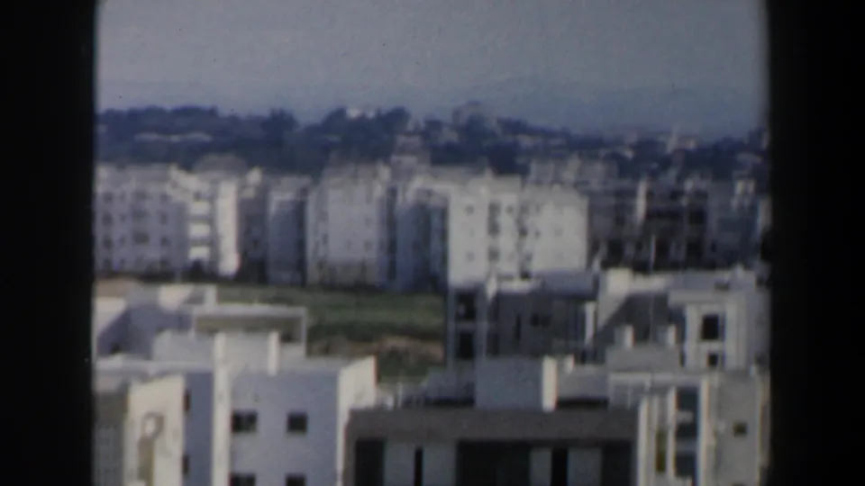 1960 Israel 8mm view over apartment buildings, open lots and a darker tree line beyond the urban edge.