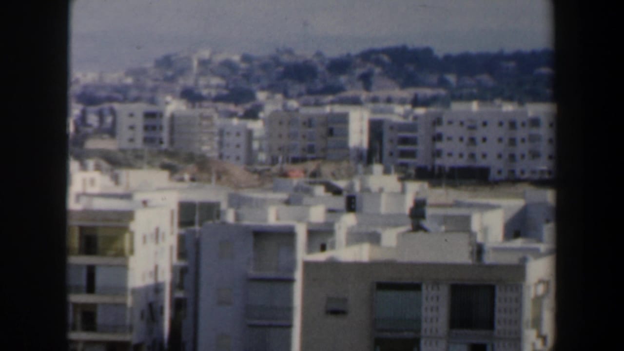 White apartment buildings and distant hillside seen in bright daylight.