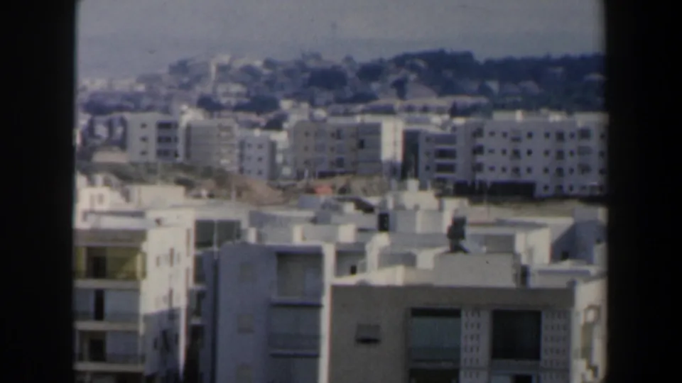 1960 Israel home-movie view of white modern apartment blocks with flat roofs and a hazy hillside beyond.