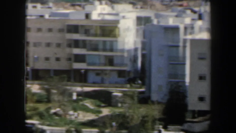 White mid-century apartment buildings in Israel, with balconies, flat roofs and a small green area visible below.