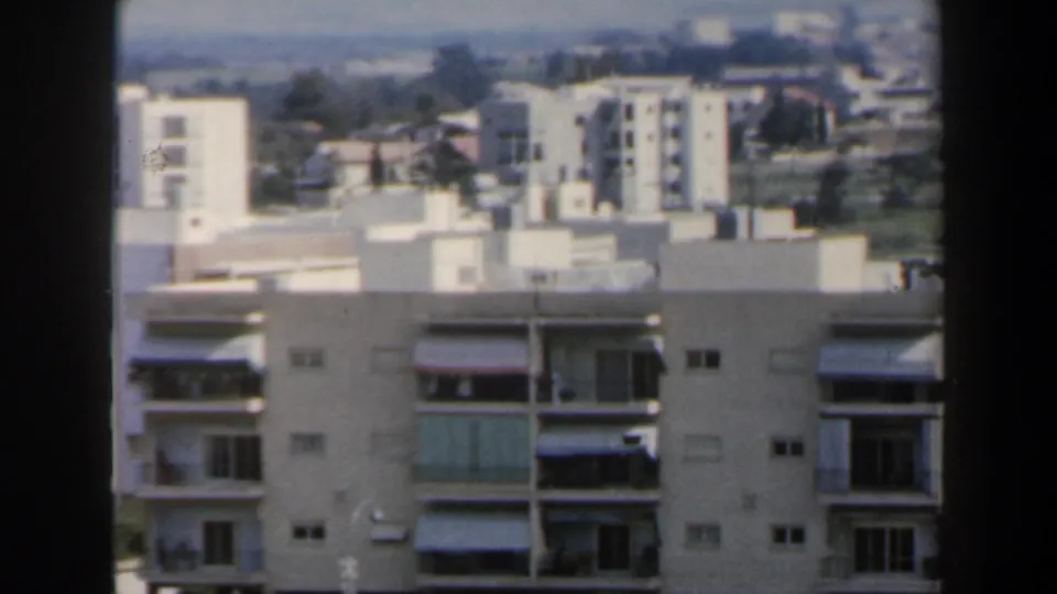 White apartment facades with balconies in a 1960 Israel city view, backed by a distant hillside neighborhood.