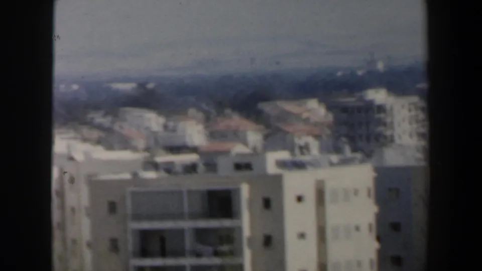 1960 Israel city-view frame with pale residential blocks, balconies, rooftops, and distant haze during a handheld pan.