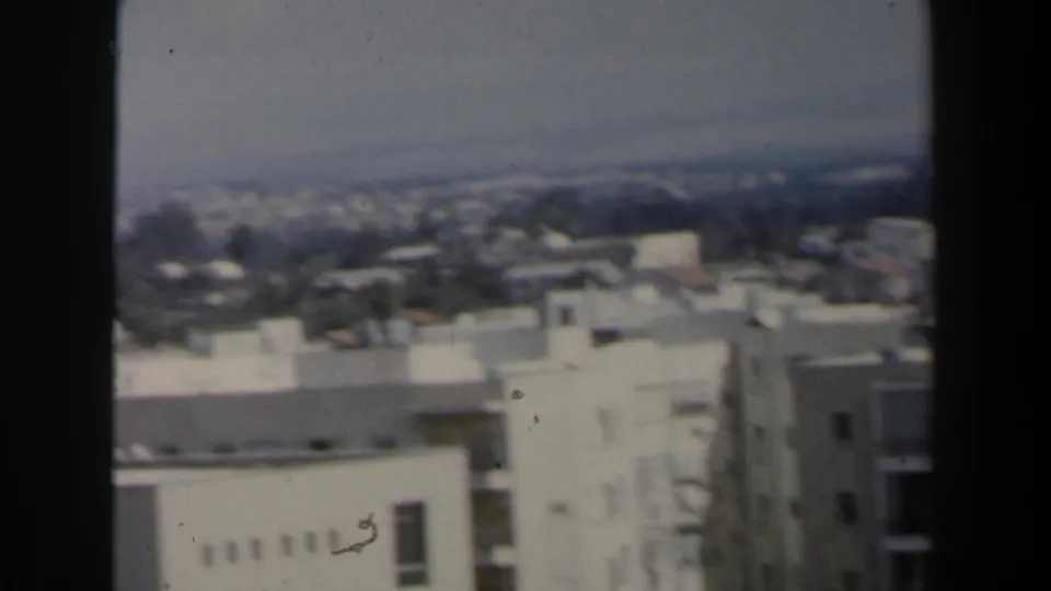 1960 Israel home-movie frame showing rooftops, apartment facades, and distant urban structures from a high vantage point.