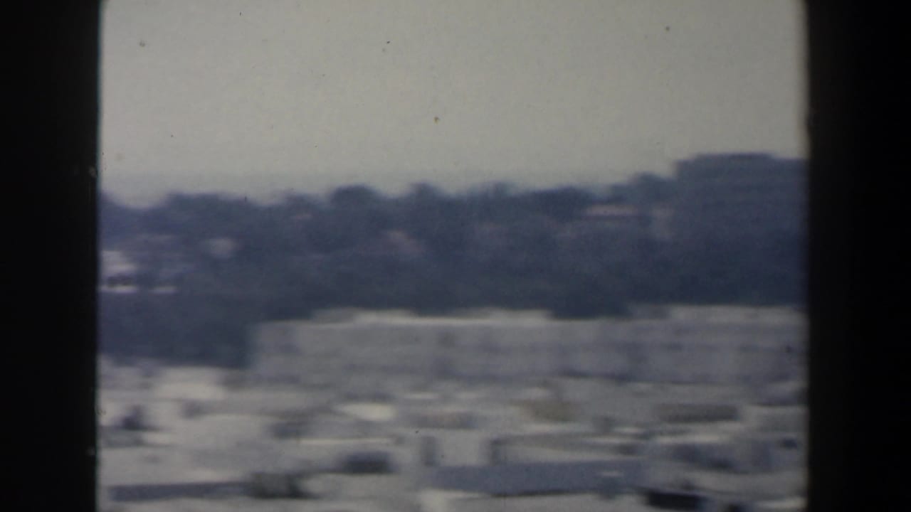 Soft city view with pale rooftops, distant trees, and dark vertical frame edges.
