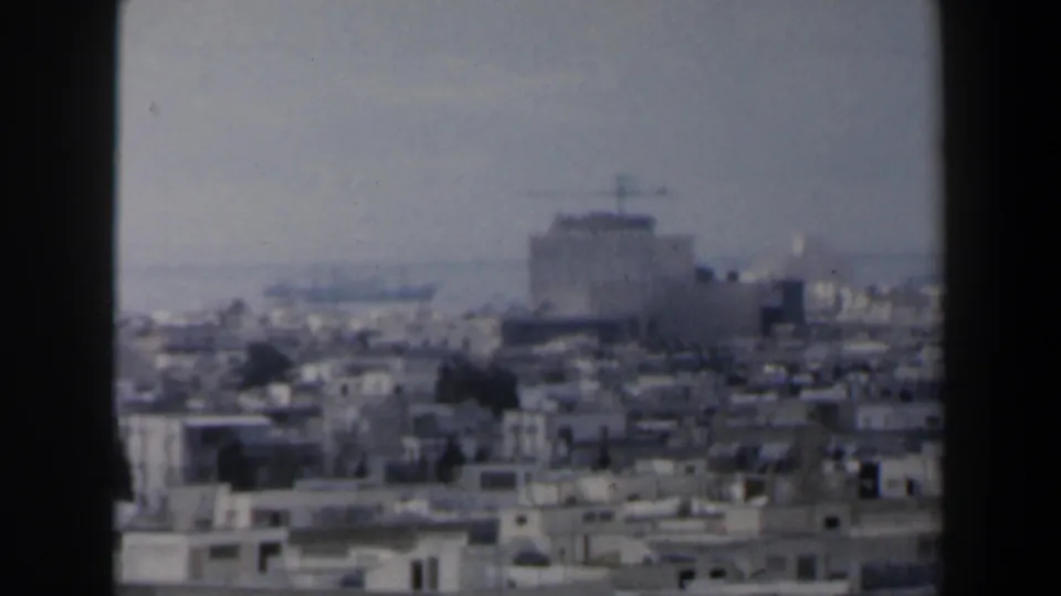 1960 Israel urban view with low rooftops, a large distant building, and a faint body of water on the horizon.