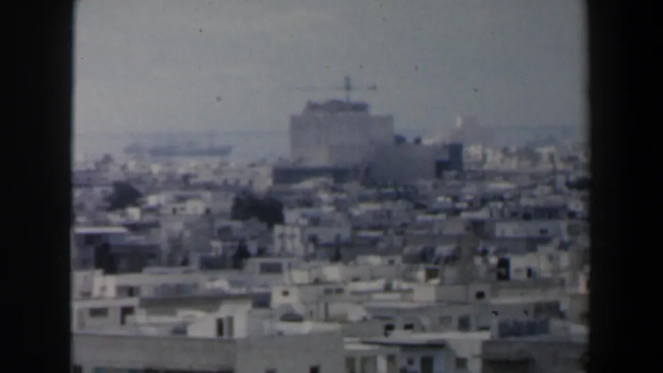 1960 Israel home-movie frame of a dense cityscape with a large building near a distant coastal horizon.