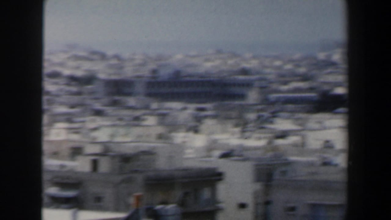 Panoramic city rooftops with a long building and distant horizon.