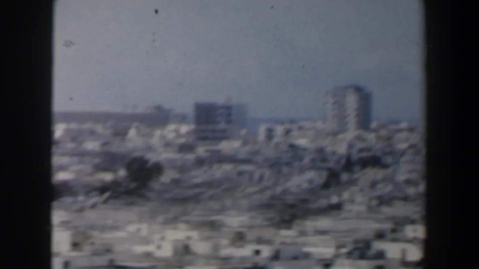 1960s Israel 8mm frame showing a distant urban skyline with low buildings and several taller blocks.