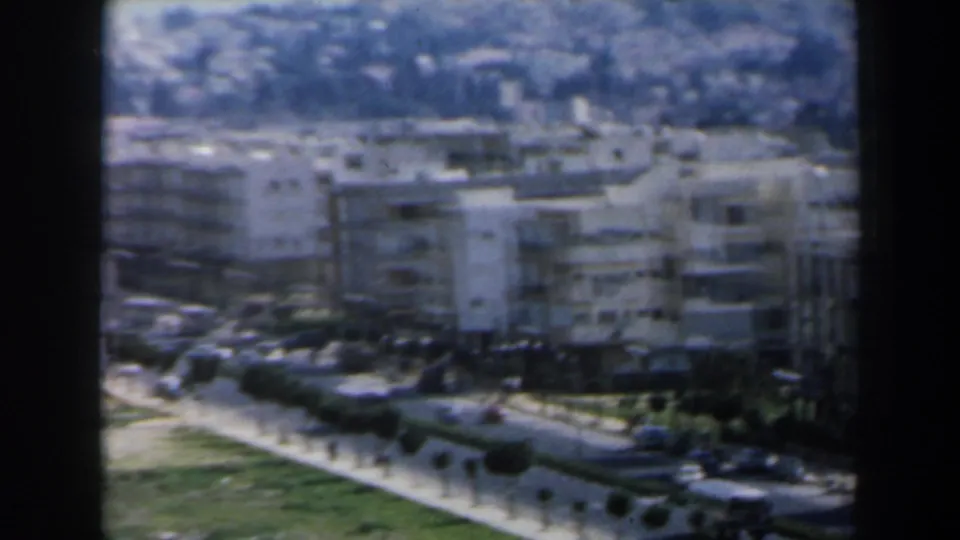 Elevated 1960 Israel view of white apartment buildings, roadside planting, cars, and a bus along a curving urban street.