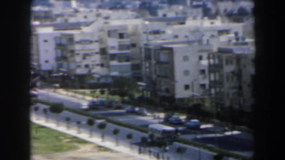 1960 Israel urban street scene with a bus, parked cars, trimmed roadside trees, grass, and mid-rise apartment buildings.