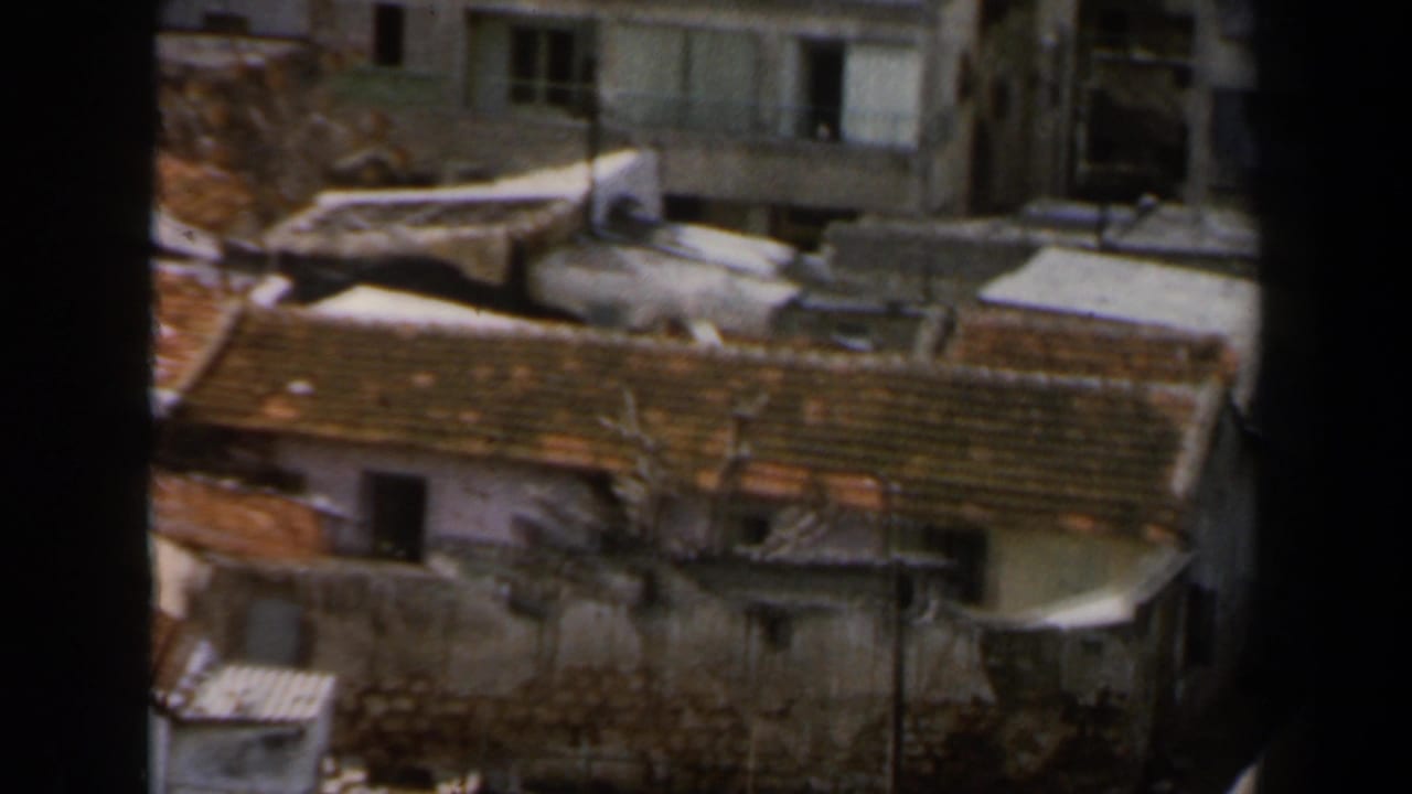 1960 8mm view in Israel showing dense rooftops, weathered walls, apartment windows, and dark foreground framing.