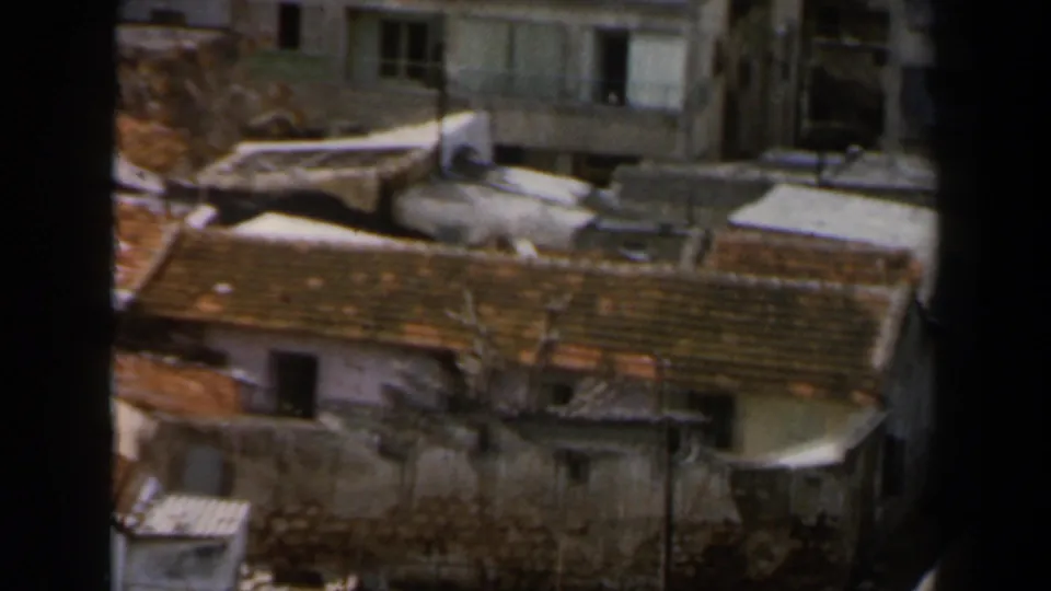 1960 8mm view in Israel showing dense rooftops, weathered walls, apartment windows, and dark foreground framing.