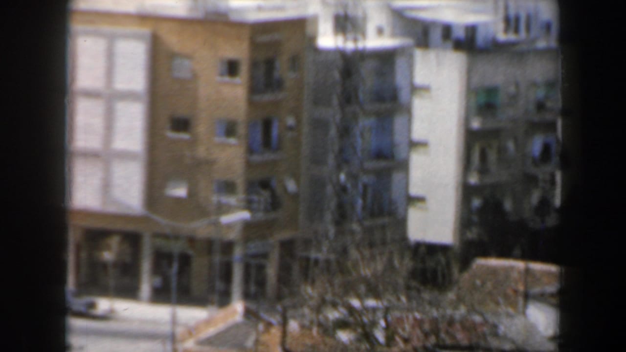 Window-framed view of apartment buildings and a city street below.