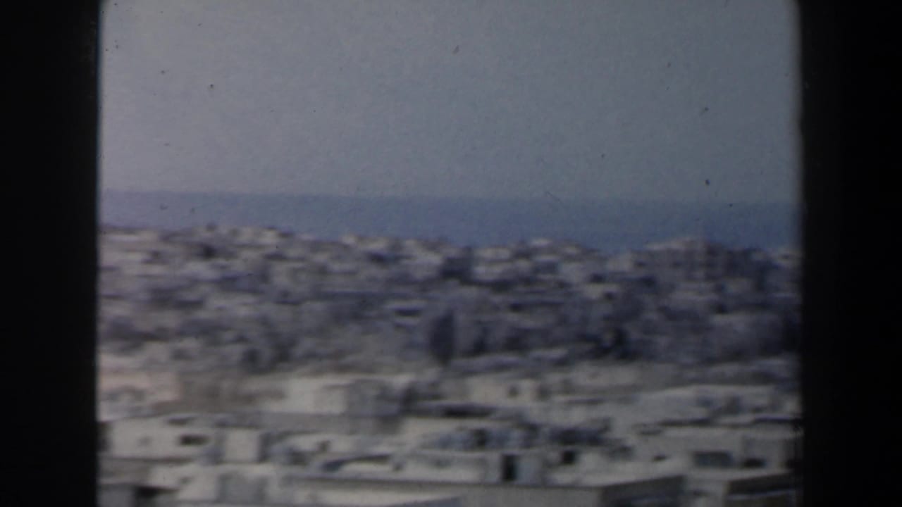 1960 Israel home-movie frame showing a soft, elevated view across dense pale urban buildings toward the sea.