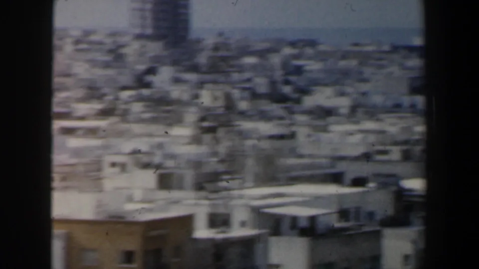 1960 Israel frame showing a blurred elevated view of dense city rooftops and a taller distant building.