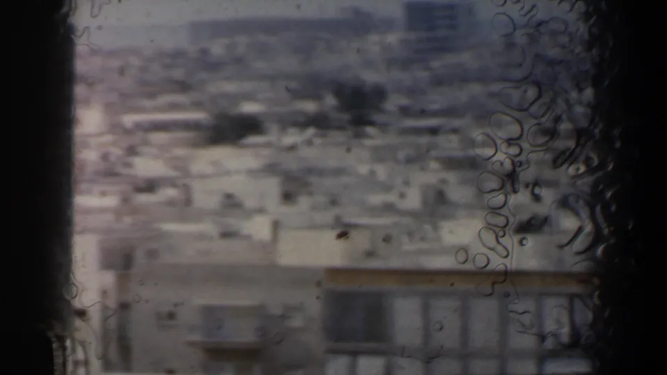 1960 Israel home-movie frame with blurred city buildings, visible film texture, and dark frame-edge borders.