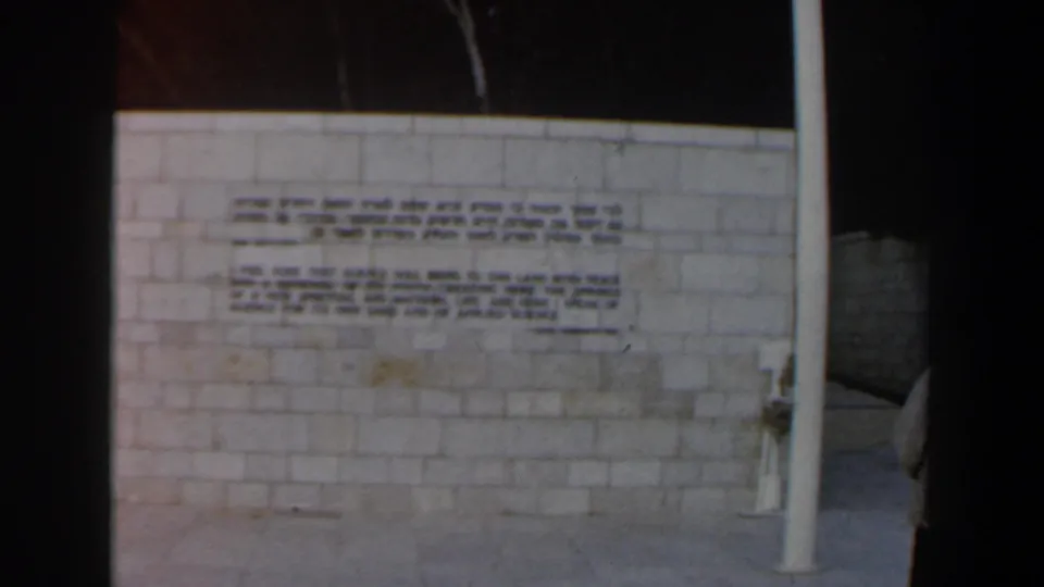 1960 Israel home-movie frame showing a pale inscribed wall with a partial visitor figure at the right edge.