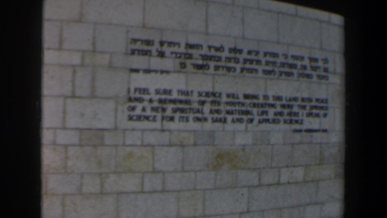 Bilingual Hebrew and English inscription on a pale stone wall within an 8mm film frame.